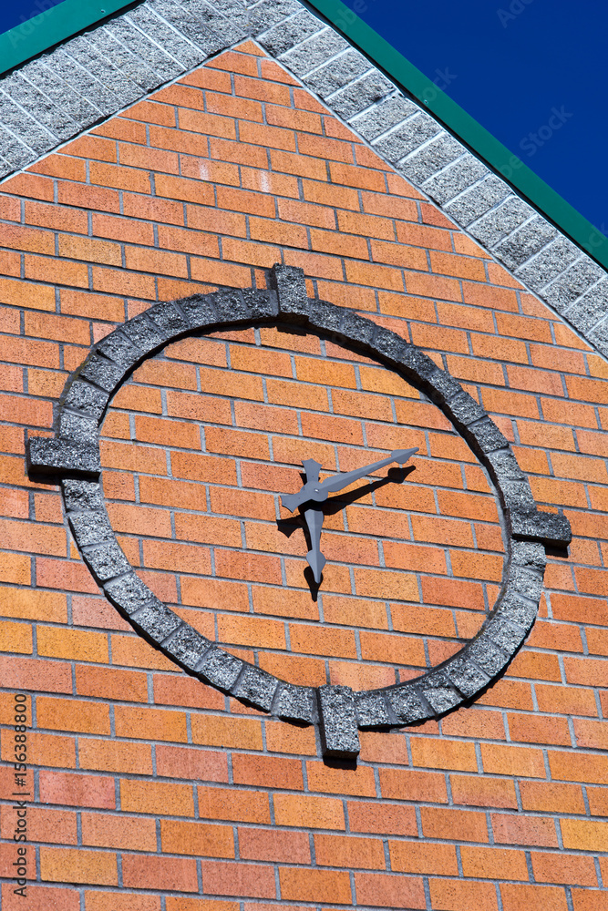 Stylized round clock on brick wall of building façade with conical roof