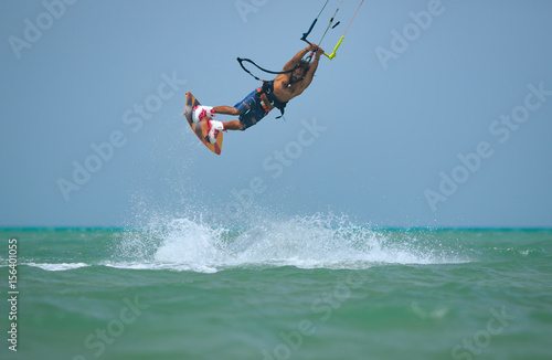 Kite boarding sportsman jumping high with kite and huge water splash and kiteboard in blue sky, active sports and life style, recreation hobby and fun, rider man on the simple air background