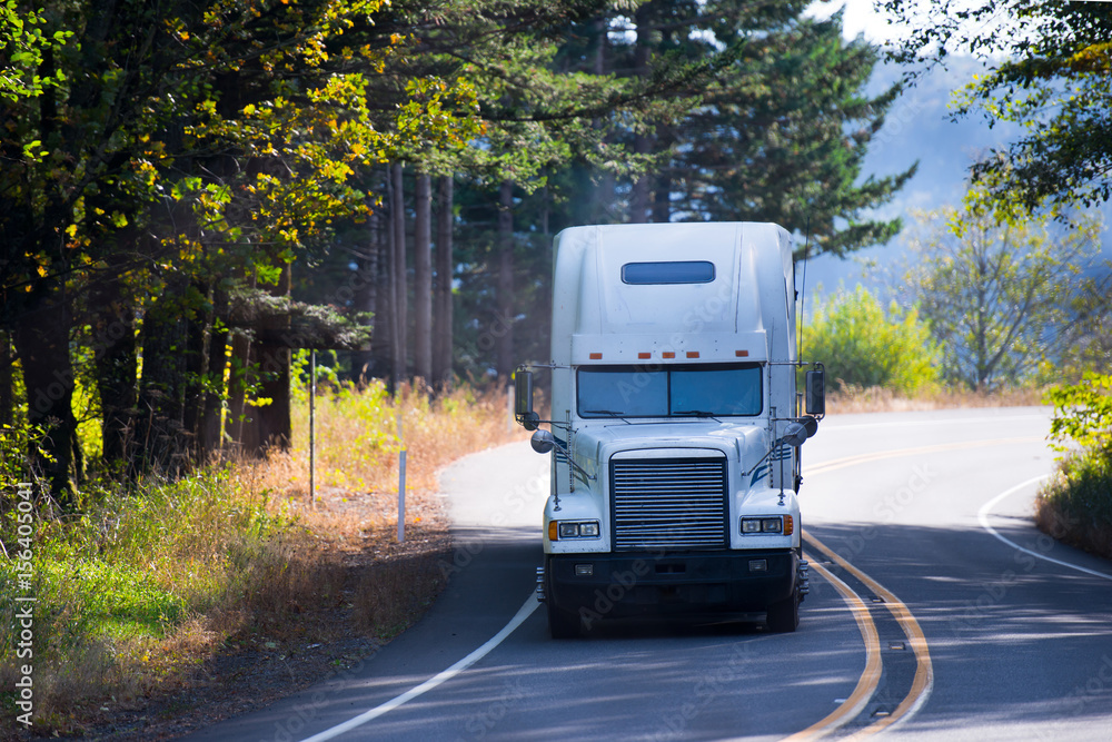 White classic semi truck big rig on winding sunny road White classic semi truck big rig on winding sunny road