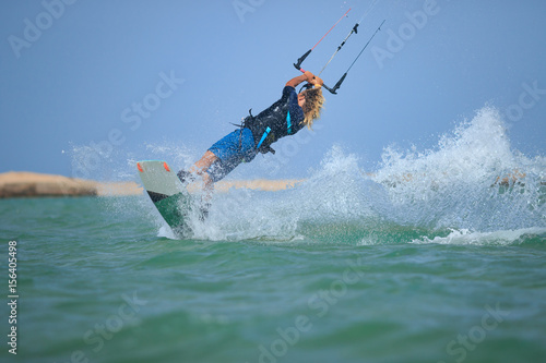 Professional kitesurfing rider sportsman jumps high acrobatics kiteboarding back mobe trick with huge water splash. Recreational activity and extreme active water sports, hobby and fun in summer time