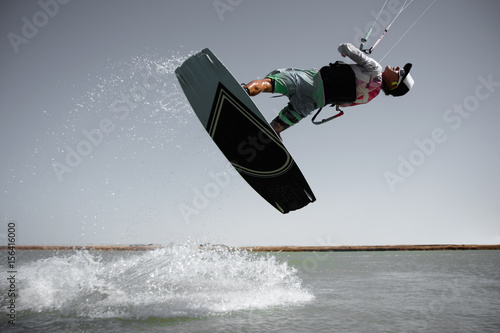 Professional kite boarding rider sportsman jumps high acrobatics kiteboarding front rotation trick tantrum with water splash. Recreational activity extreme active water sports