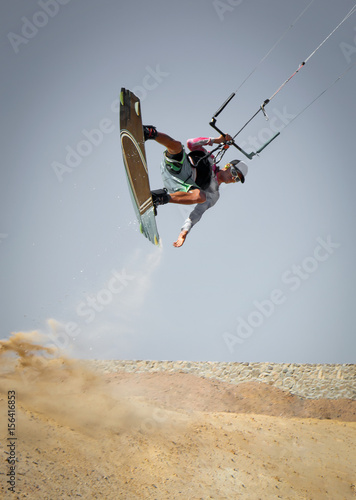 Kiter rides across the land. Professional kite boarding sportsman slides with board in desert sands and stones, extreme sport. Recreational activity and extreme active water sports, hobby and fun time