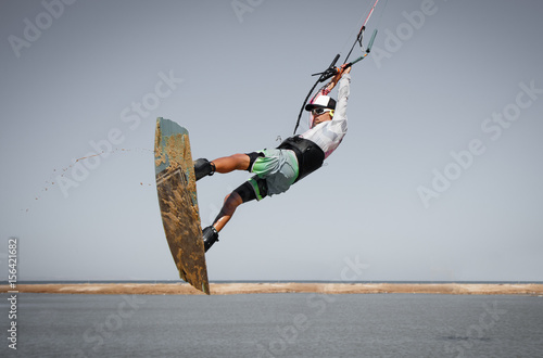 Professional kitesurfer  rider sportsman jumps high acrobatics kiteboarding trick with front rotation from sand into water. Recreational activity and extreme active water sports, hobby and fun time
