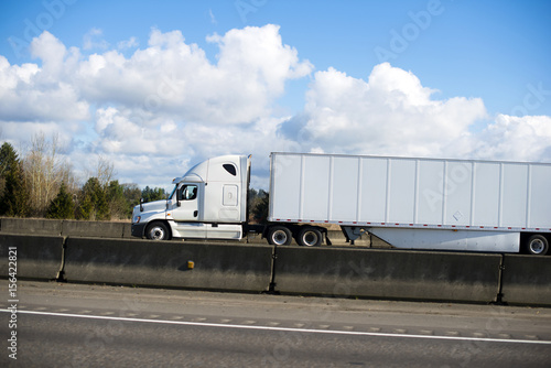 Excellent modern white semi truck trailer dry van on highway with concrete border and cloud sky side view