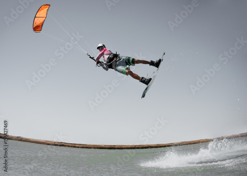 Professional kite boarding rider sportsman jumps high acrobatics kiteboarding raley trick  with water splash. Kitesurfer flies high. Recreational activity and extreme active water sports, hobby, fun