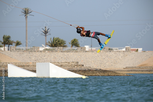 Wakeboarding sportsman young rider jumping high from the kicker obstacle in the wake boarding cablepark, active sports and life style, recreation and fun, active hobby and life style, water sports photo