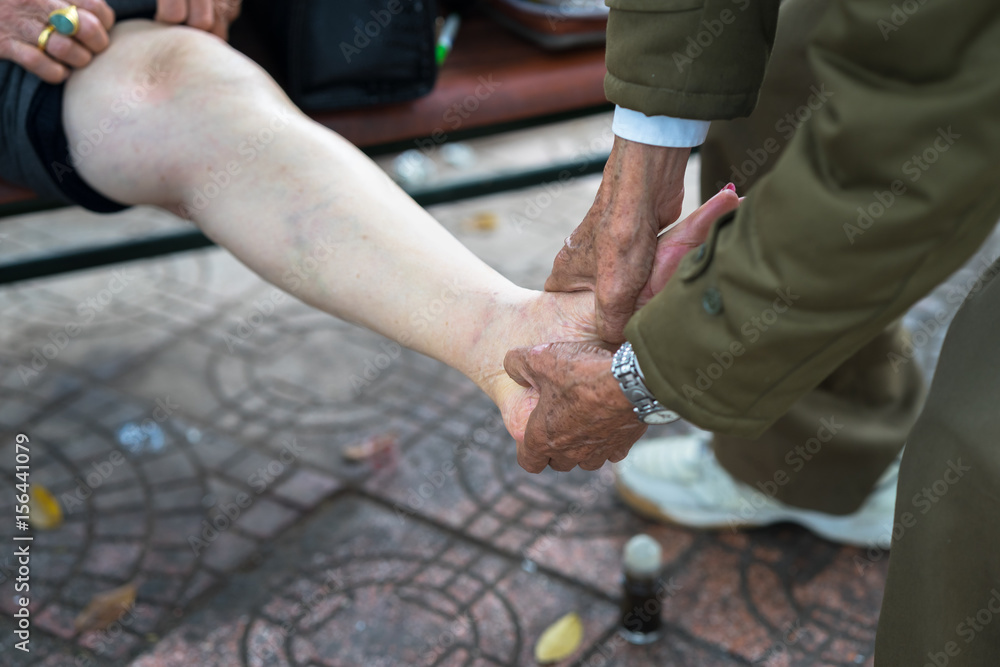 Fototapeta premium Senior man hands doing massage on old woman pain legs on street