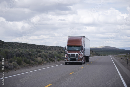 Brown modern semi truck with trailer driving long Nevada highway