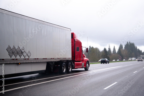Red modern semi truck transporting cargo trailer on highway