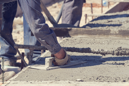Construction worker leveling concrete pavement outdoors.