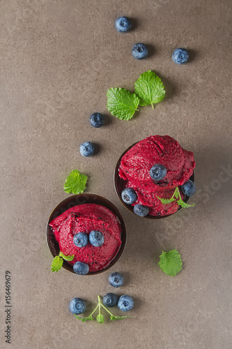 Frozen red sorbet, berry ice cream in a blue cup with mint and blueberries. Gray background. Space for text.Top view