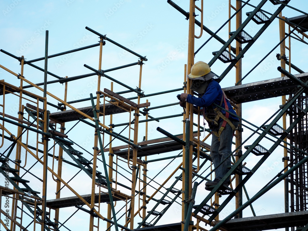Construction workers working on scaffolding, Man Working on the Working at height with blue sky at construction site Construction workers working on scaffolding, Man Working on the Working at height with blue sky at construction site