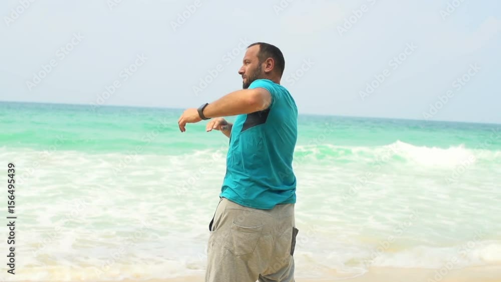 Young man exercising, doing warmup on tropical beach
