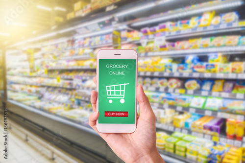 woman hand holding mobile with grocery online on screen with blur supermarket background