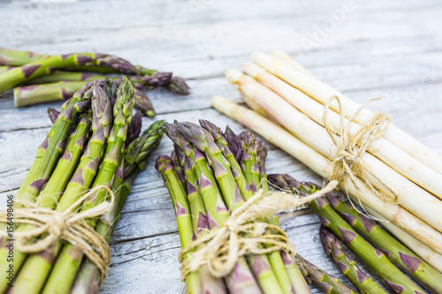 Fresh and raw green and white asparagus bunches on a wooden background. 