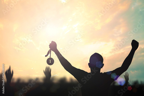 Victory concept: Silhouette human hand holding gold medal against colorful autumn sunset sky photo