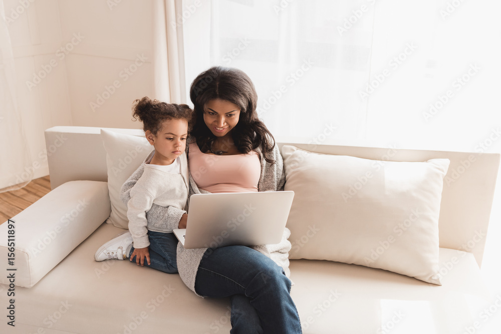 Beautiful mother and daughter sitting on couch and using laptop together Beautiful mother and daughter sitting on couch and using laptop together