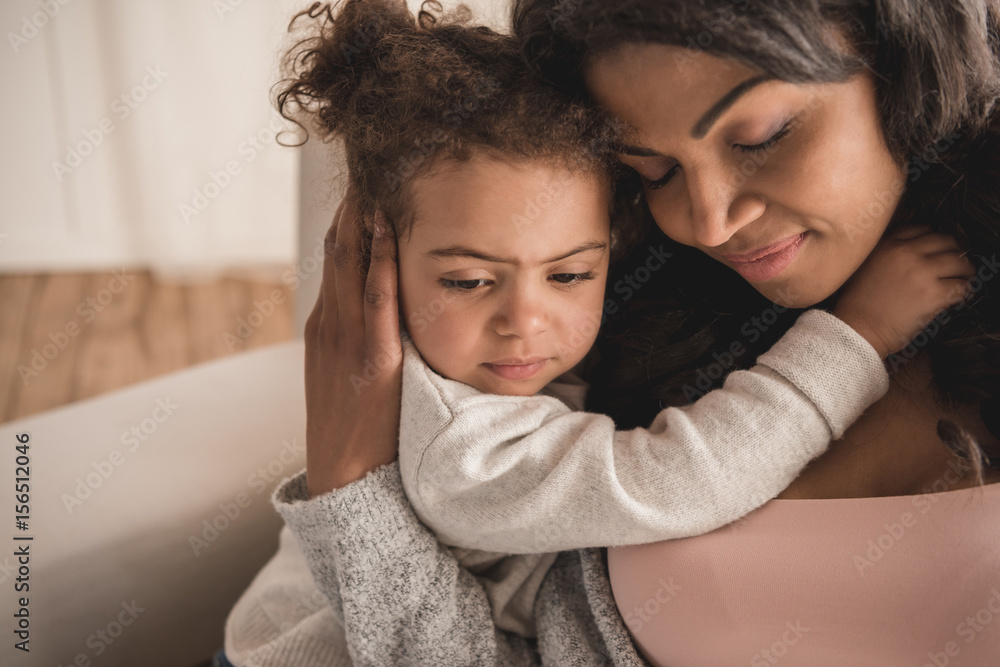 Obraz premium Close-up portrait of beautiful african american mother and daughter hugging at home