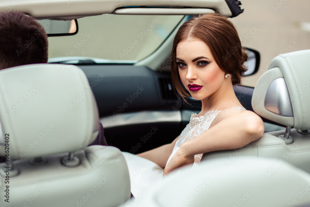gorgeous bride with fashion makeup and hairstyle in a luxury wedding dress with handsome groom near white cabriolet car