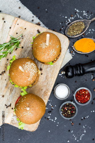 Three beef burger craft on a wooden board on stone pavement, spices, rosemary, pepper, rock salt, turmeric, chili, dried basil, fast food, fashion, colorful