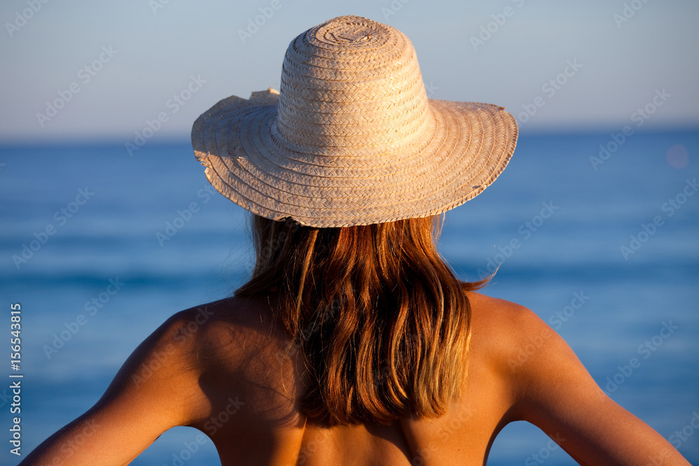 femme de dos face à la mer avec un chapeau de paille Photos | Adobe Stock