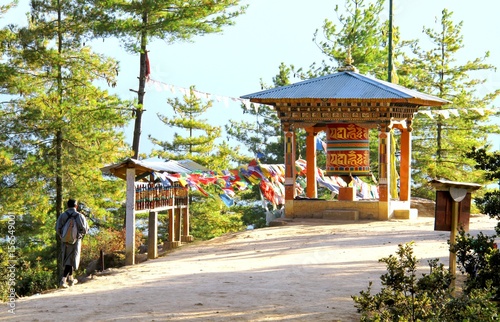Bhutanese man in traditional cloth walking near the prayer wheels and colorful Tibetan prayer flags on the path to Taktshang Goemba or Tiger's nest monastery, Paro, Bhutan.