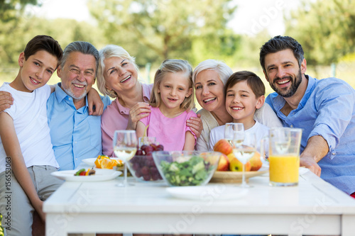 Family sitting at table outdoors, smiling 