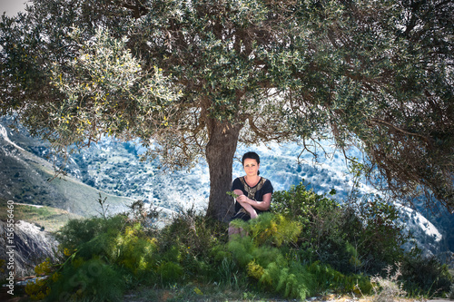 Brunette girl under an olive tree on a background of mountains. Fantastic landscape. Olive oil, olive, fairy tale, elf, fairy, Greek, Athena, Aphrodite, Goddess. Myths of ancient Greece and Rome.