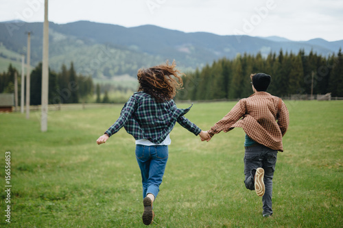 Couple of lovers holding hands and running away in mountains. Woman and man in love walking outdoors. 