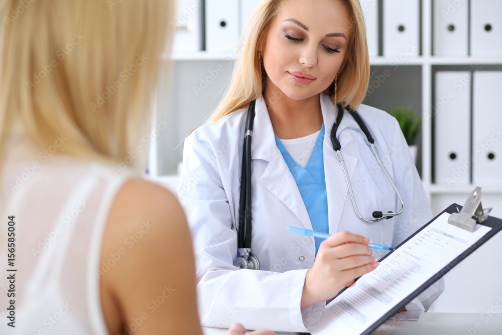 Doctor and patient discussing something while physician pointing into medical history form at clipboard Doctor and patient discussing something while physician pointing into medical history form at clipboard