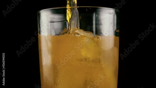 Slow mo. Filled glass with orange drink with ice cubes juice soda on black background