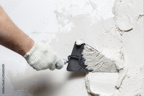 Construction worker puts a gypsum on the wall with a spatula photo