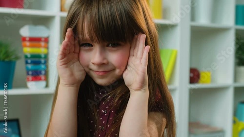 Cute little girl covers her face with hands. Playing hide and seek, peek a boo. Close up
