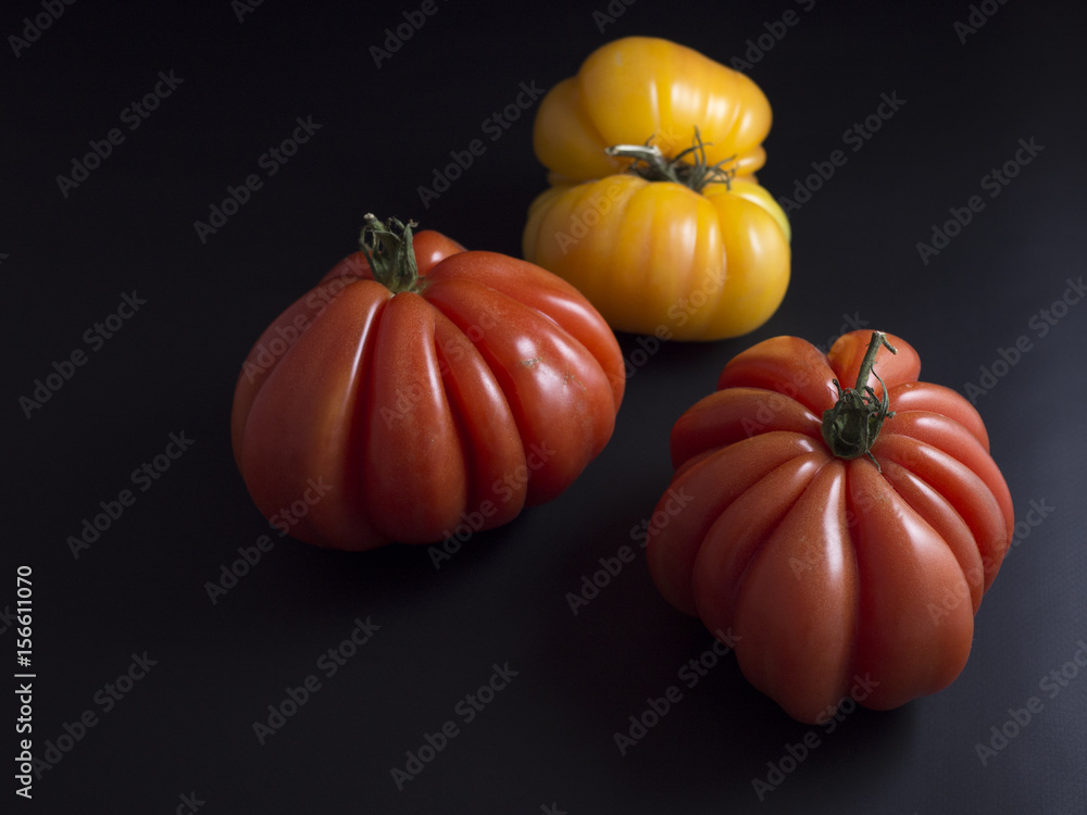 Obraz premium Three big red and yellow beef tomatoes with green stems isolated on black background
