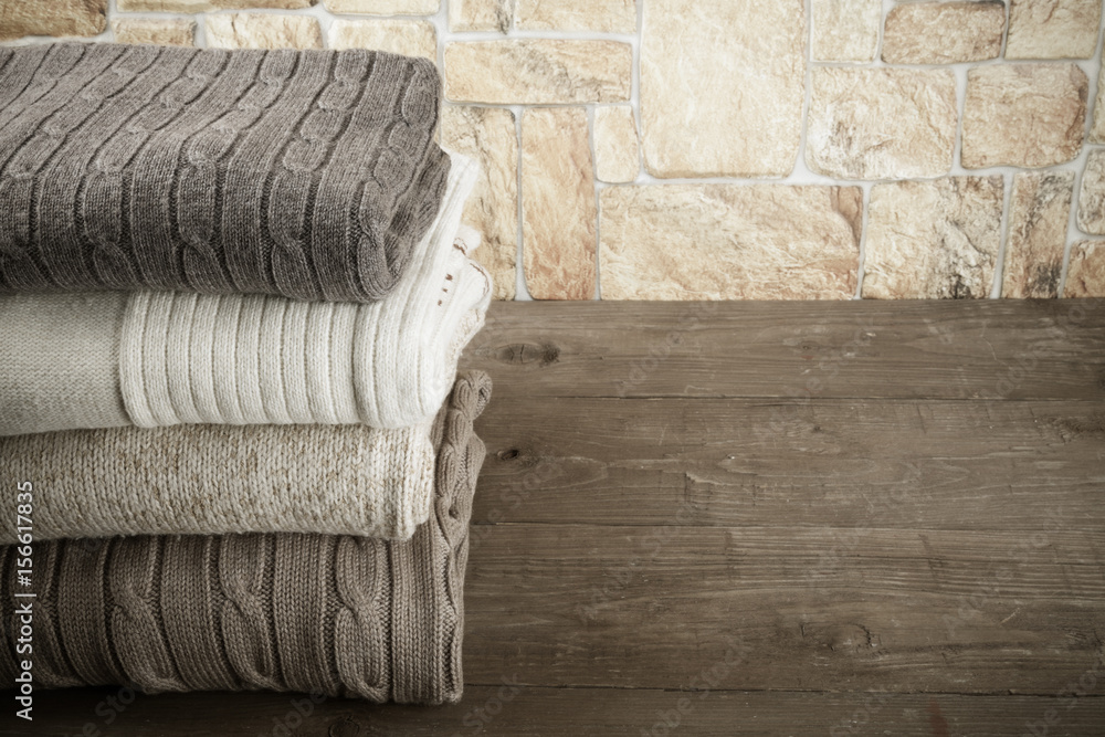 Stack of knitting clothes on wooden table opposite a stony wall. Toned Stack of knitting clothes on wooden table opposite a stony wall. Toned