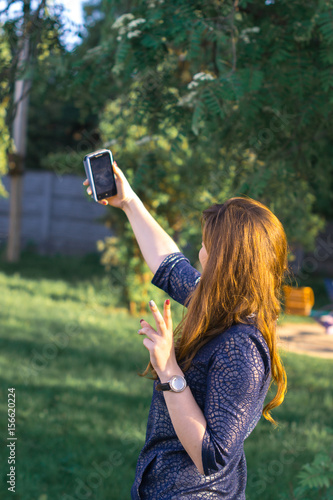 Beautiful girl doing selfie on phone in park.