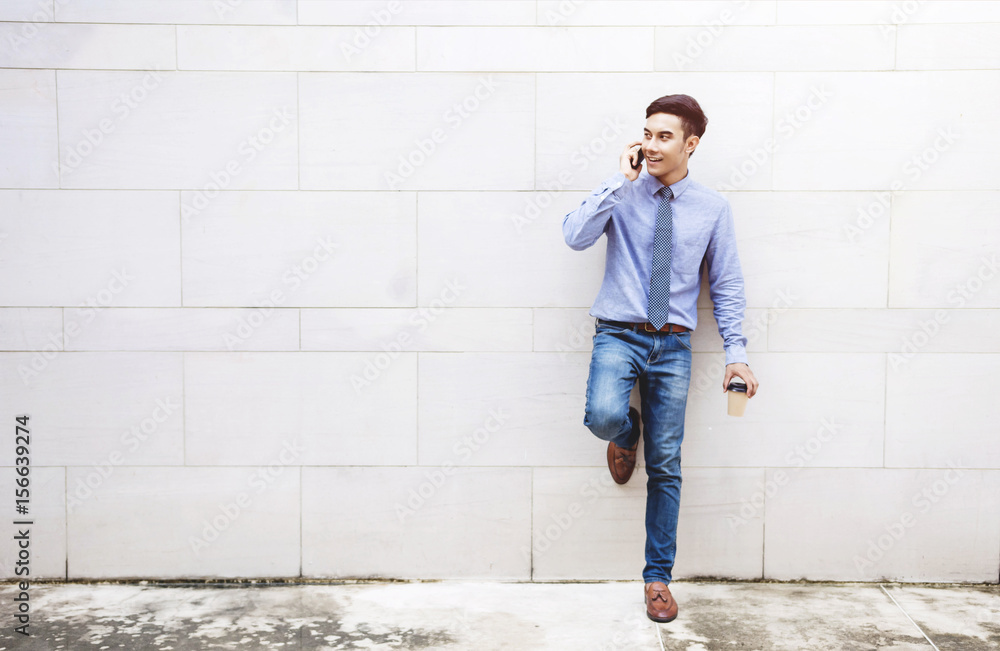Young and modern attractive Businessman stand and talk via Smart phone outside building wall, Social communicate technology in business concept, Lifestyle of modern male Young and modern attractive Businessman stand and talk via Smart phone outside building wall, Social communicate technology in business concept, Lifestyle of modern male