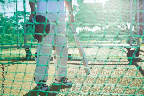 Low section of cricketer standing by net at field