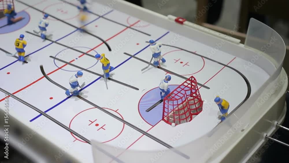 Person playing table ice hockey, hitting puck into opposing net, indoor activity Person playing table ice hockey, hitting puck into opposing net, indoor activity