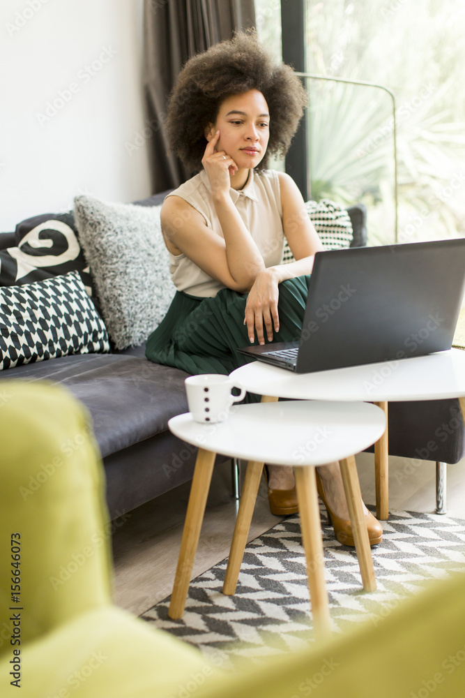 Young woman with curly hair, uses laptop and sitting on the sofa at home Young woman with curly hair, uses laptop and sitting on the sofa at home
