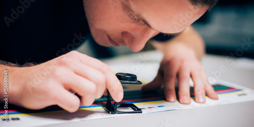 Worker in printing and press centar uses a magnifying glass photo