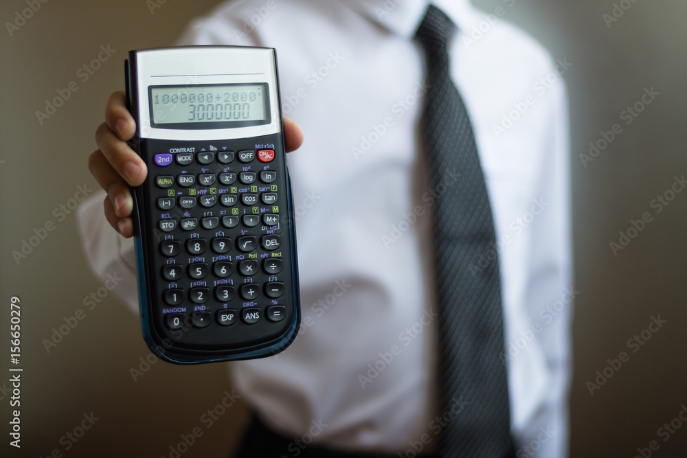 Young businessman in a white shirt and tie with a calculator in his hand. The boy shows a calculator with a figure of 3000000 Young businessman in a white shirt and tie with a calculator in his hand. The boy shows a calculator with a figure of 3000000