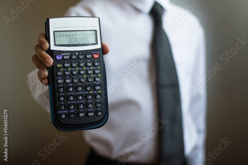 Young businessman in a white shirt and tie with a calculator in his hand. The boy shows a calculator with a figure of 3000000