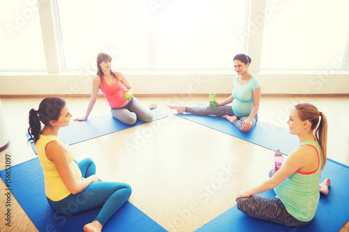 happy pregnant women sitting on mats in gym