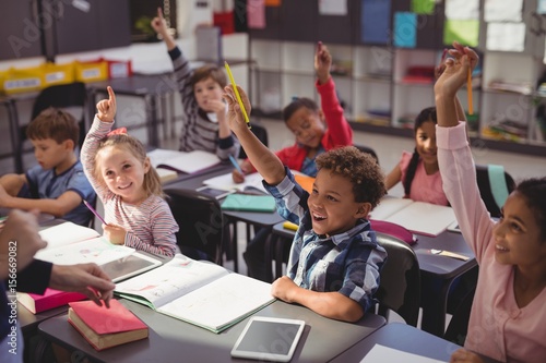Schoolkids raising their hands in classroom photo