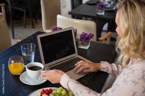 Woman holding coffee cup while using laptop 