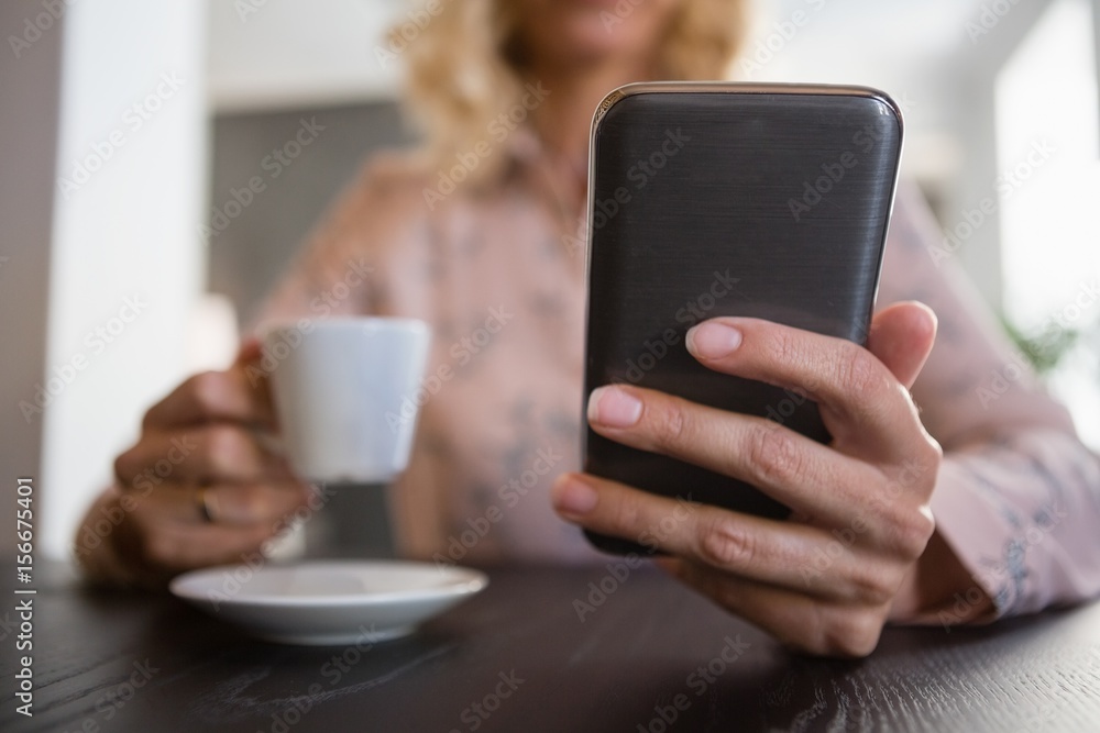 Businesswoman using mobile phone while having coffee in cafe Businesswoman using mobile phone while having coffee in cafe
