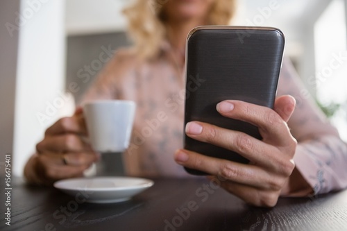 Businesswoman using mobile phone while having coffee in cafe
