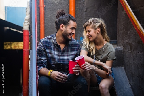 Happy couple interacting while having drink on staircase