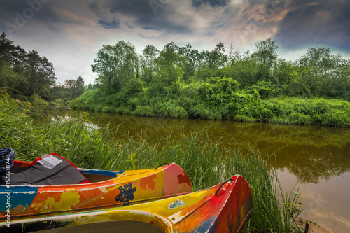 Kayaks sitting on a green grassy riverbank.